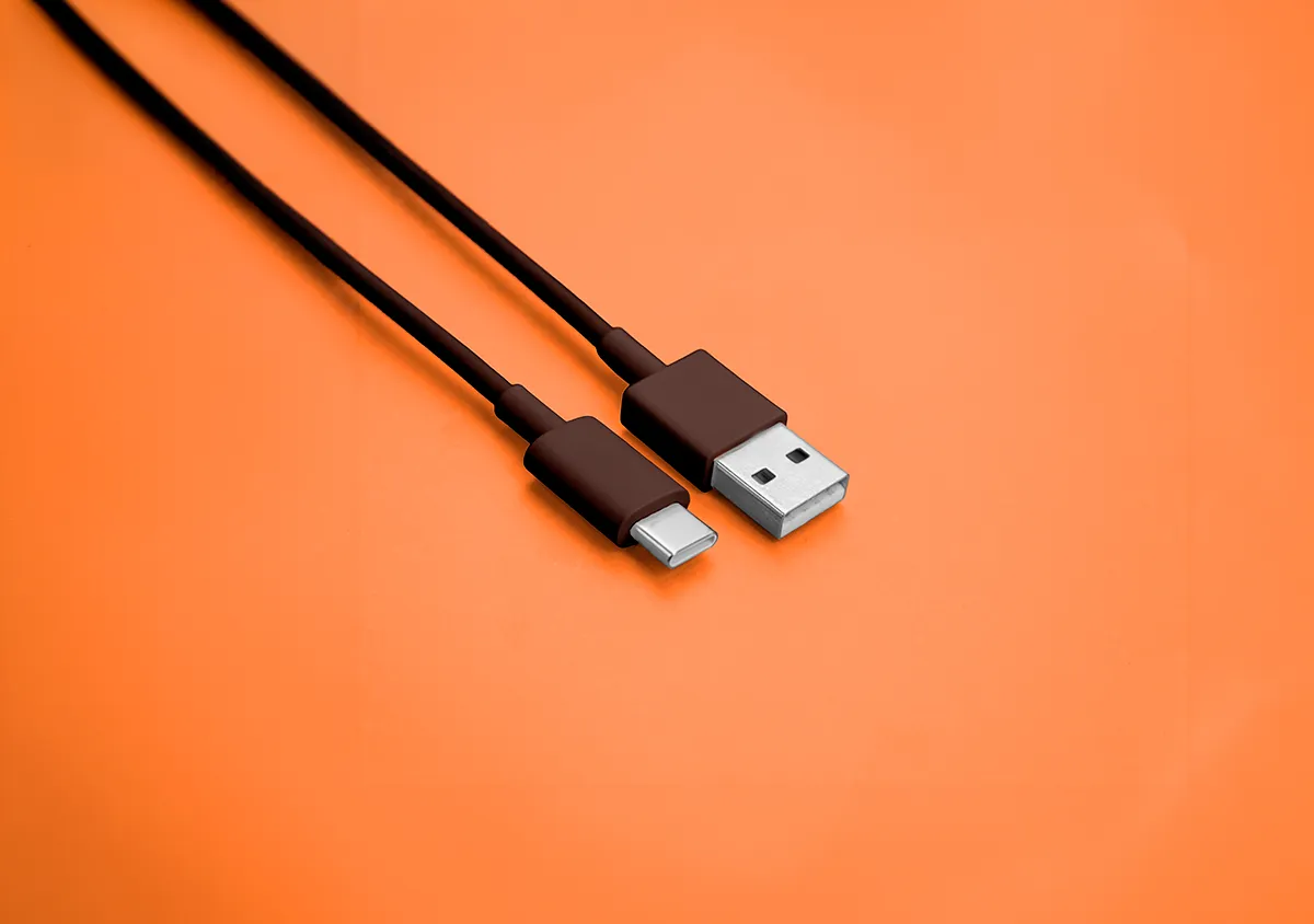 Cable USB-C junto a conector USB tradicional sobre fondo naranja representando la nueva normativa europea de conectividad tecnológica