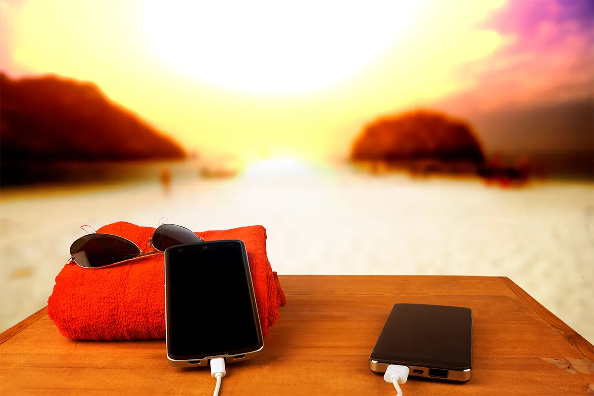 Smartphone expuesto al calor del verano junto a una batería externa sobre una mesa de madera