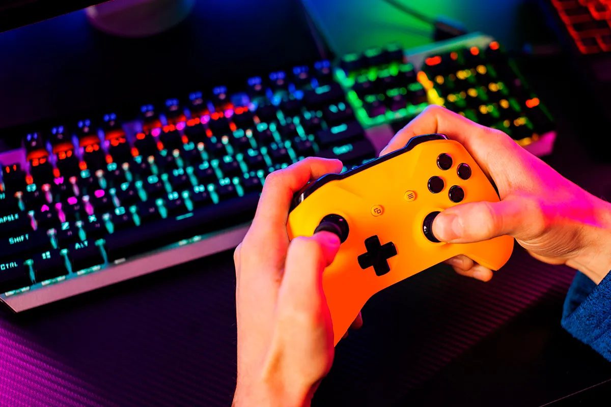 Persona jugando con un mando frente a un ordenador para ilustrar el crecimiento de la industria del videojuego en Cataluña.